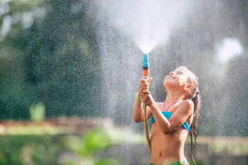 Cute little girl pours herself from the hose, makes a rain. Hot summer day pleasure
