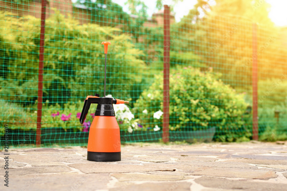 pressure sprayer bottle with measured scale on blurred background of green garden.