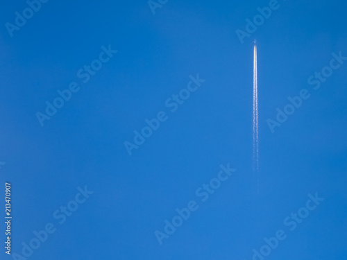 A jet airplane far away climbing fast with a long double white trail in a pretty clear blue sky, with a tree canopy in the bottom of the photo near the photographer © JArmando_ClauEleone