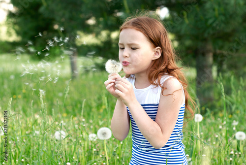 Beautiful red-headed girl, blowing with concentration of an dandelion in a summer forest.