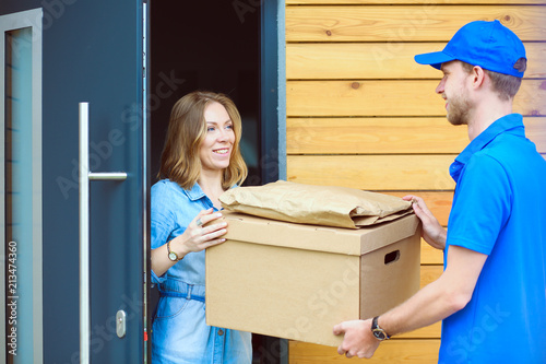 Smiling delivery man in blue uniform delivering parcel box to recipient - courier service concept. Smiling delivery man in blue uniform