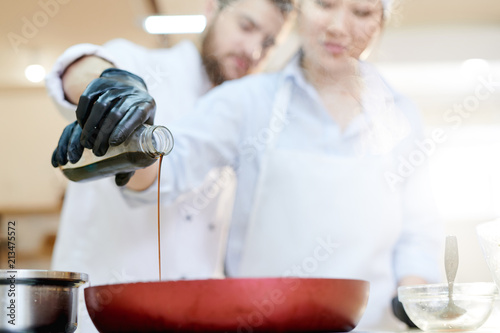 Close up of two professional cooks working in restaurant kitchen poring soy sauce into frying pan, focus on foreground, copy space