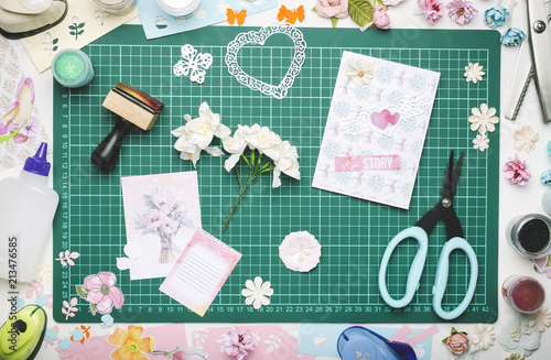 Paper flowers, a homemade card and tools for scrapbooking on the green mat for cutting. The view from the top, no hands