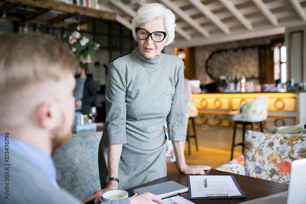 Senior business leader standing and explaining the plan of work to her colleague at the restaurant Senior business leader standing and explaining the plan of work to her colleague at the restaurant