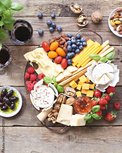 Cheese platter with fresh berries and nuts on a rustic wooden table. Overhead view.