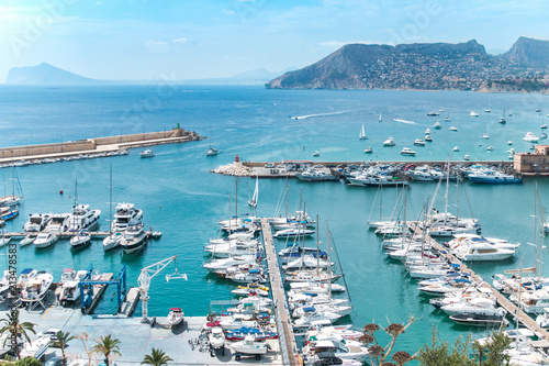 Top view of the marina, port with many boats, some moored, others sail on the sea. In the distance a picturesque mountain with many houses. The city of Calpe in Spain, Valencia, Europe.