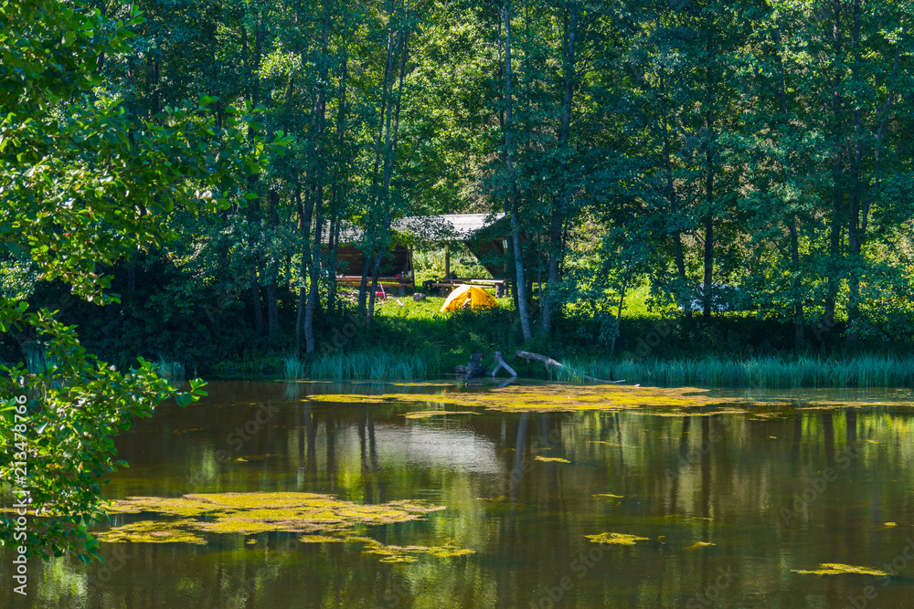 A small pond with water-lilies growing in it with tents on the green grass on the opposite shore. With tourists in them tourists. A small pond with water-lilies growing in it with tents on the green grass on the opposite shore. With tourists in them tourists.
