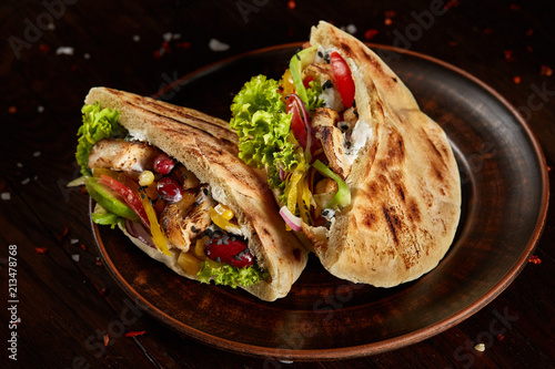 Pita stuffed with chicken, beans and letucce on clay plate over wooden background, side view, selective focus.