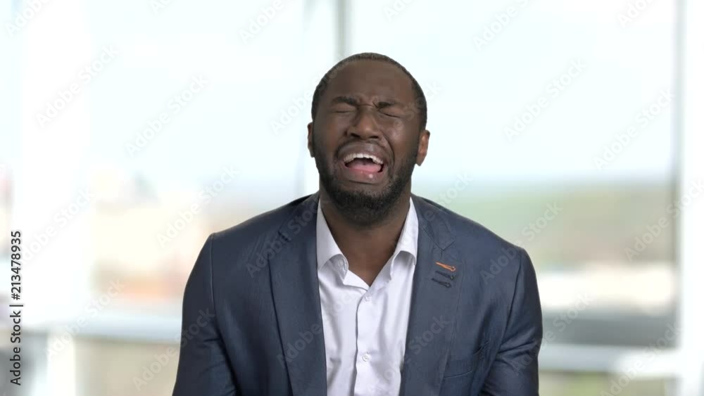 Frustrated crying black business man in suit. Indoor, office windows background.