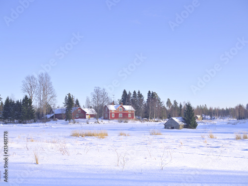 Beautiful view at old abandoned countryside houses by a snow covered field on a sunny winter day.