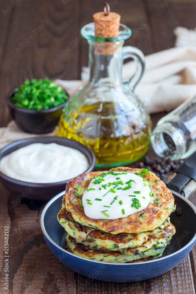 Vegetarian zucchini fritters or pancakes, served with greek yogurt and green onion on wooden background, vertical