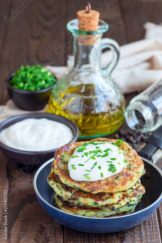 Vegetarian zucchini fritters or pancakes, served with greek yogurt and green onion on wooden background, vertical