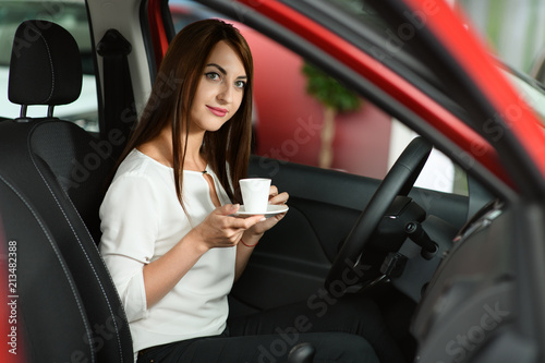 Beautiful girl is drinking coffee in the new car.