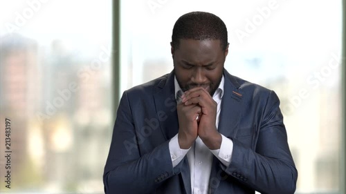 Portrait of black african business man praying to god. Sorrowful black man in suit indoor, checkered windows background.