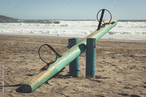 Green wooden seesaw on sand in La Serena beach, Chile. Kids playground teeter totter. Vintage effect