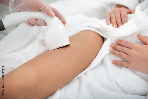 Close up female arm doing depilation of legs for young client with gadget. Skin care concept
