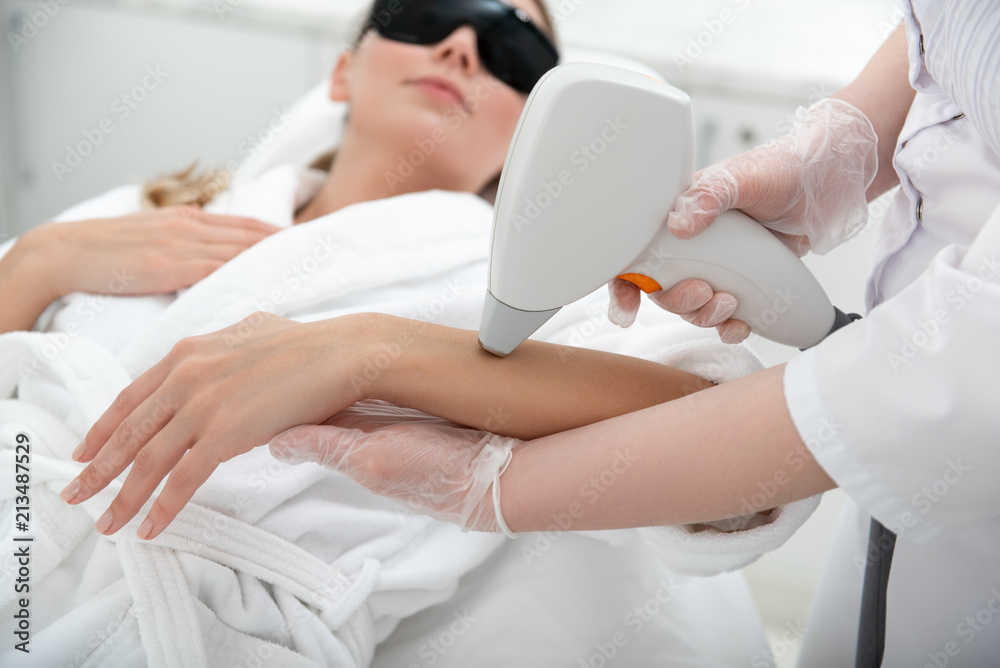 Orderly girl having hair removal. Cosmetologist doing it with digital device