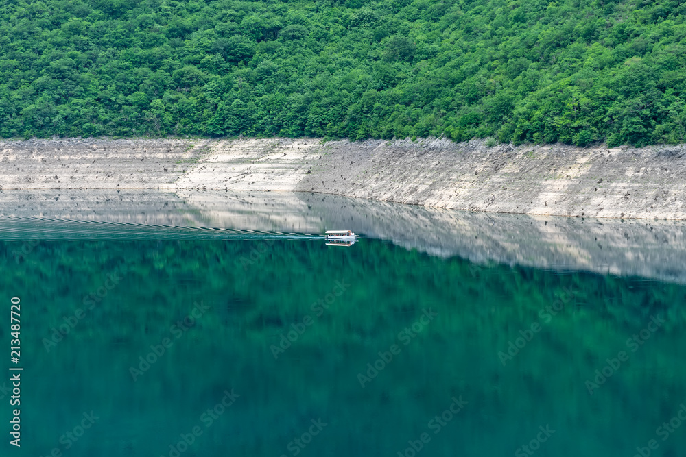 A sightseeing boat with tourists swims along the picturesque lake among the canyon.