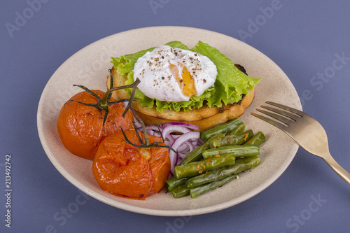 Poached egg on a piece of bread with fried green beans, tomato and arugula on a plate