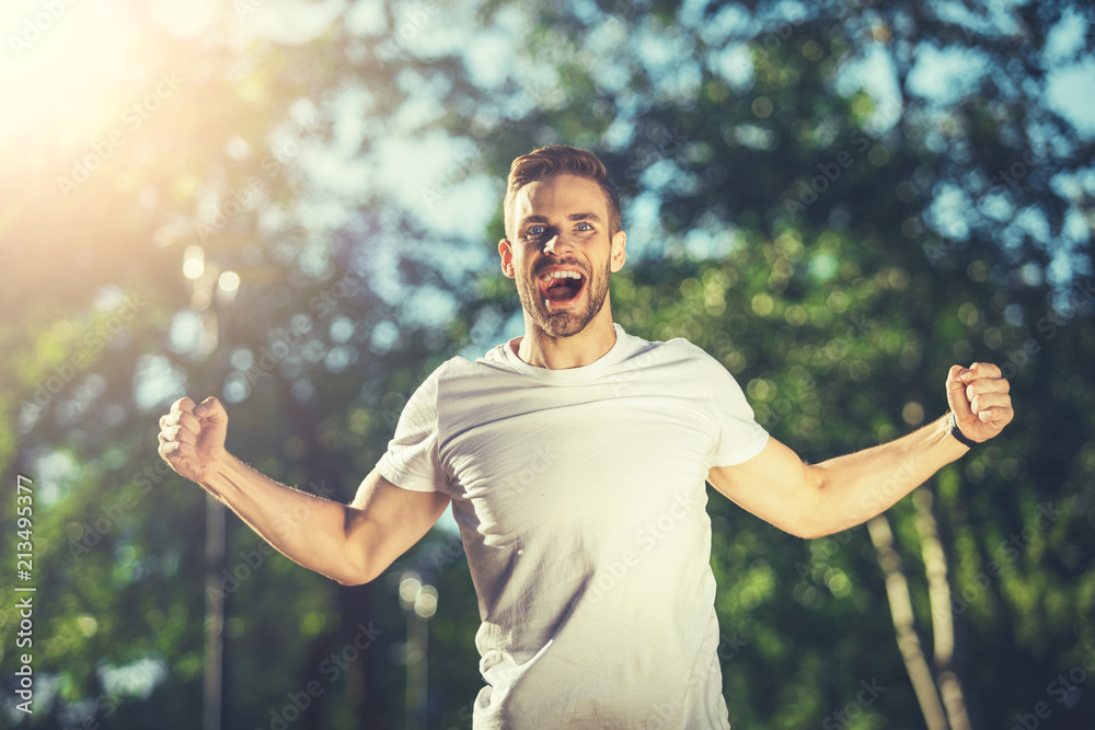 Obraz premium Waist up portrait of screaming man standing outside with stretched hands and smiling. He is enjoying sport and physical activity outside