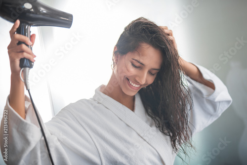 Portrait of cheerful female blowing wind on hair after taking shower. She gesticulating hands and having fun