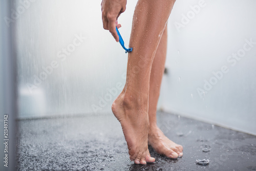 Close up woman hand shaving calf while relaxing in shower. Drops of water falling around her photo