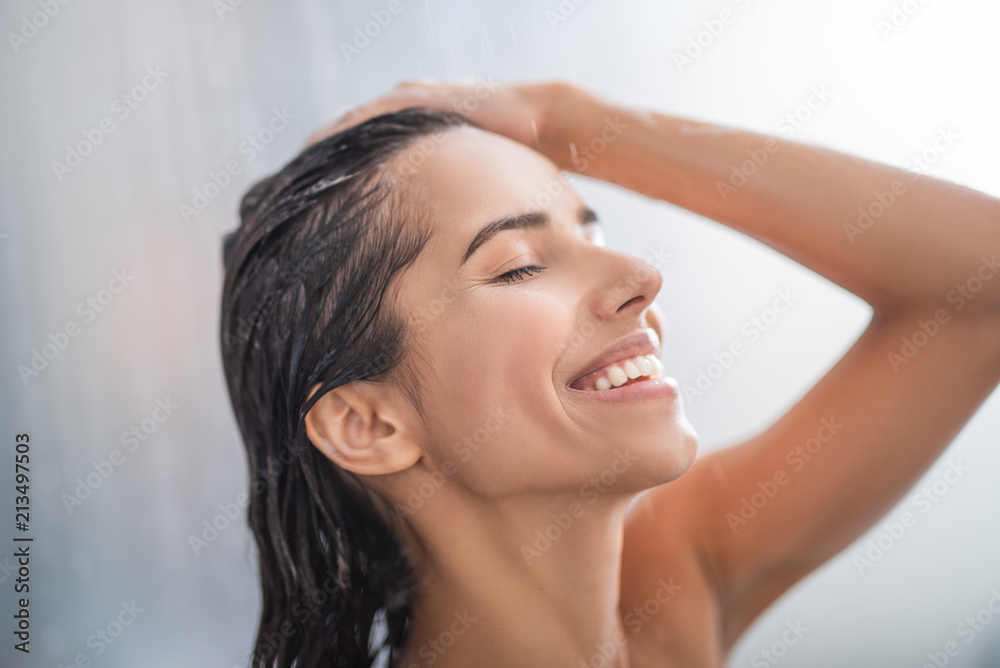 Side view beaming lady relaxing under stream of water. She keeping head with hand Side view beaming lady relaxing under stream of water. She keeping head with hand