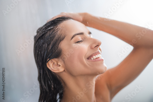 Side view beaming lady relaxing under stream of water. She keeping head with hand