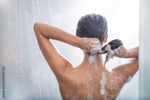 Lady washing hair while relaxing under stream of water. She gesticulating hands photo