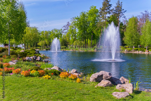 A small pond with a pair of fountains in a green, spring park