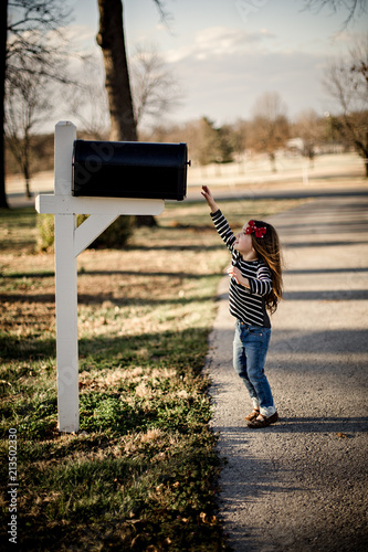 Little girl dressed stylish reaching for large mailbox above her. 
