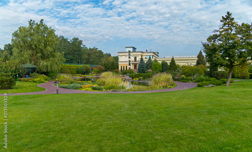 A beautiful decorative lake with a huge number of different shrubs and decorative flower beds in the background of a modern building A beautiful decorative lake with a huge number of different shrubs and decorative flower beds in the background of a modern building