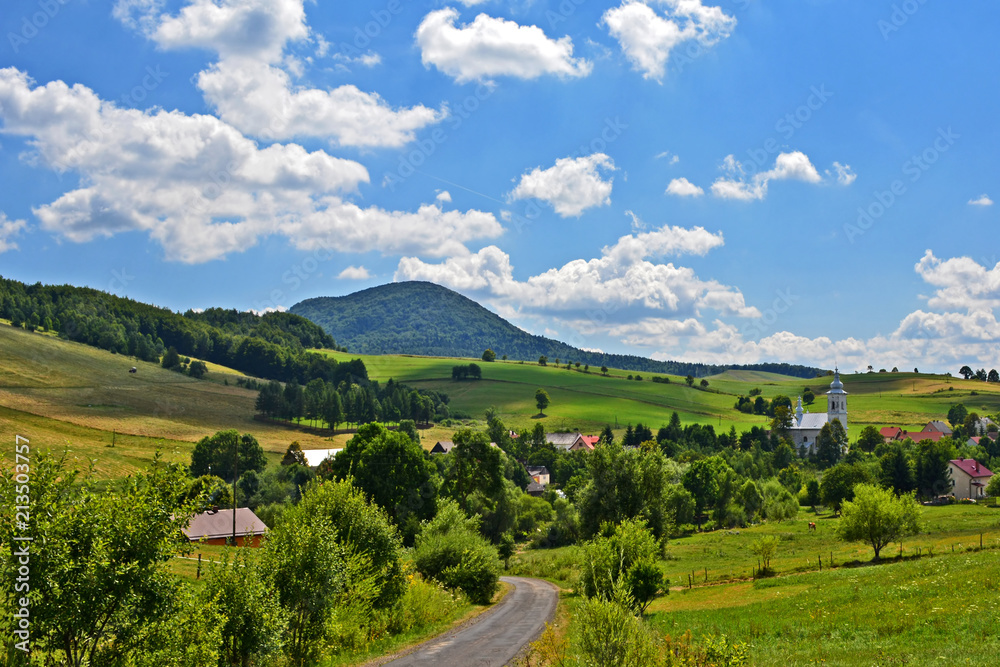 View of  grass fields,  church in Izby village and mountain Lackowa (997 msl) in Low Beskid (Beskid Niski), Poland