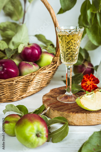 Apple cider in a glass and a decanter and basket with ripe apples on a wooden table in vintage style