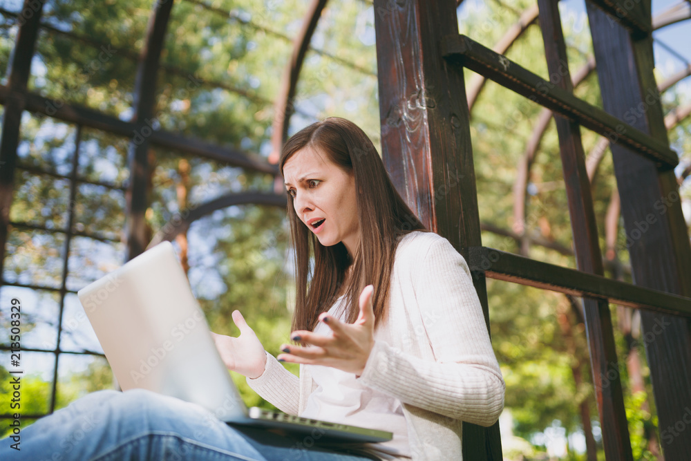 Young successful businesswoman in light casual clothes. Shocked Woman working on modern laptop pc computer in city park in street outdoors on spring nature. Mobile Office. Freelance business concept. Young successful businesswoman in light casual clothes. Shocked Woman working on modern laptop pc computer in city park in street outdoors on spring nature. Mobile Office. Freelance business concept.