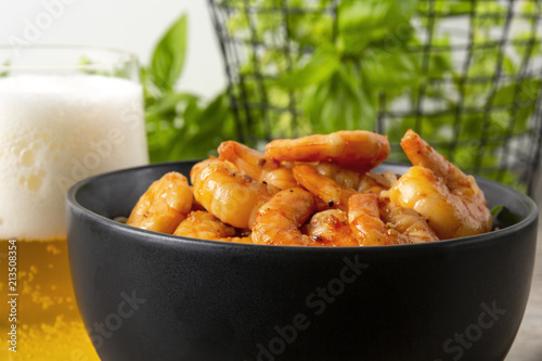 Fried prawns in a black bowl and beer. On a background basket with greens. Eastern food.