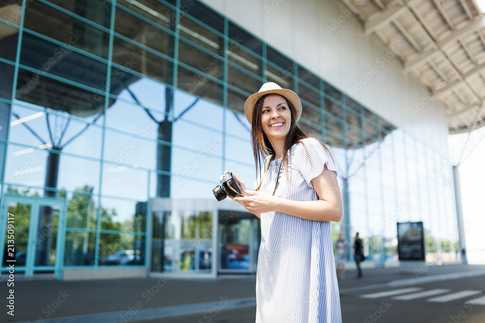Young joyful traveler tourist woman holding retro vintage photo camera, looking aside at international airport. Female passenger traveling abroad to travel on weekends getaway. Air flight concept.