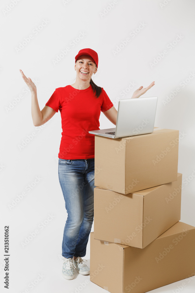 Full length portrait of delivery young woman in red cap, t-shirt isolated on white background. Female courier standing near empty cardboard boxes with laptop pc computer. Receiving package. Copy space Full length portrait of delivery young woman in red cap, t-shirt isolated on white background. Female courier standing near empty cardboard boxes with laptop pc computer. Receiving package. Copy space