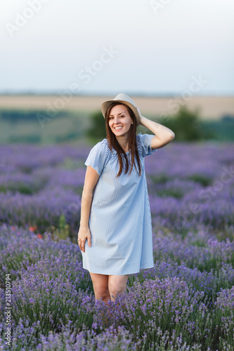 Fototapeta Naklejka Na Ścianę i Meble -  Portrait of young sensual beautiful woman in blue dress, hat on purple lavender flower blossom meadow field outdoors on summer nature, Provence. Tender female near flowering bush. Lifestyle concept.