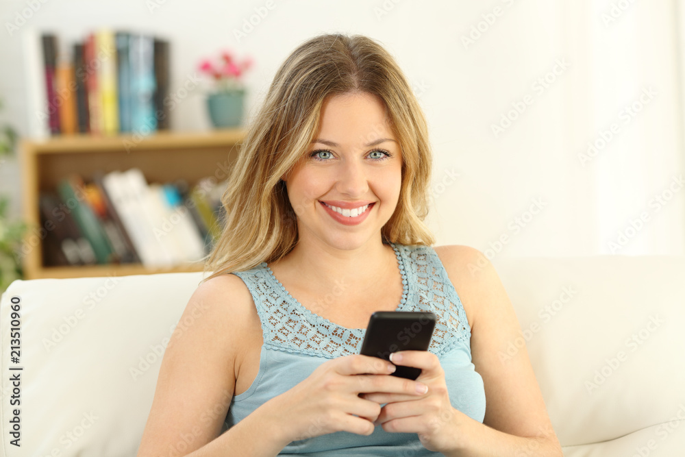 Happy woman holding phone and looking at camera at home Happy woman holding phone and looking at camera at home