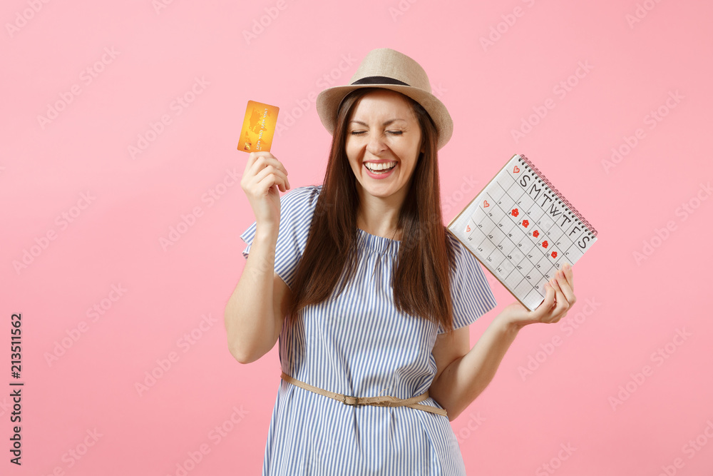 Portrait of happy woman in blue dress, hat holding credit card, periods calendar, checking menstruation days isolated on trending pink background. Medical healthcare gynecological concept. Copy space.