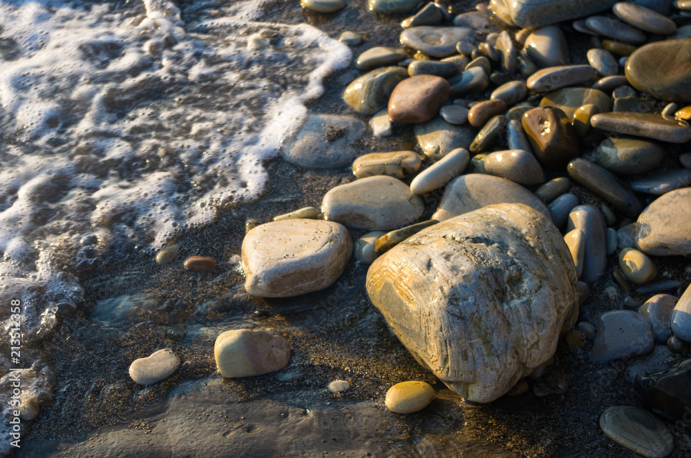 pebble stones on the sea beach, the rolling waves of the sea with foam