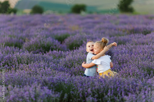 Playful little cute couple boy girl walk on purple lavender flower meadow field background, have fun, play, enjoy good sunny day. Excited small kids. Family day, children, childhood lifestyle concept.
