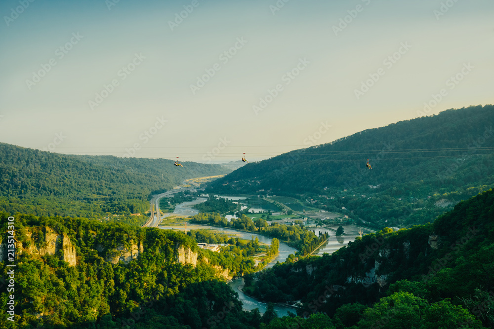 Fototapeta premium People enjoy the pleasure of skiing on an extreme cable car over the gorge overlooking the stunning scenery of the mountains, the sky and the river. Extreme entertainment and recreation.