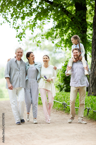 Cheerful family in casualwear walking down road in natural environment during chill