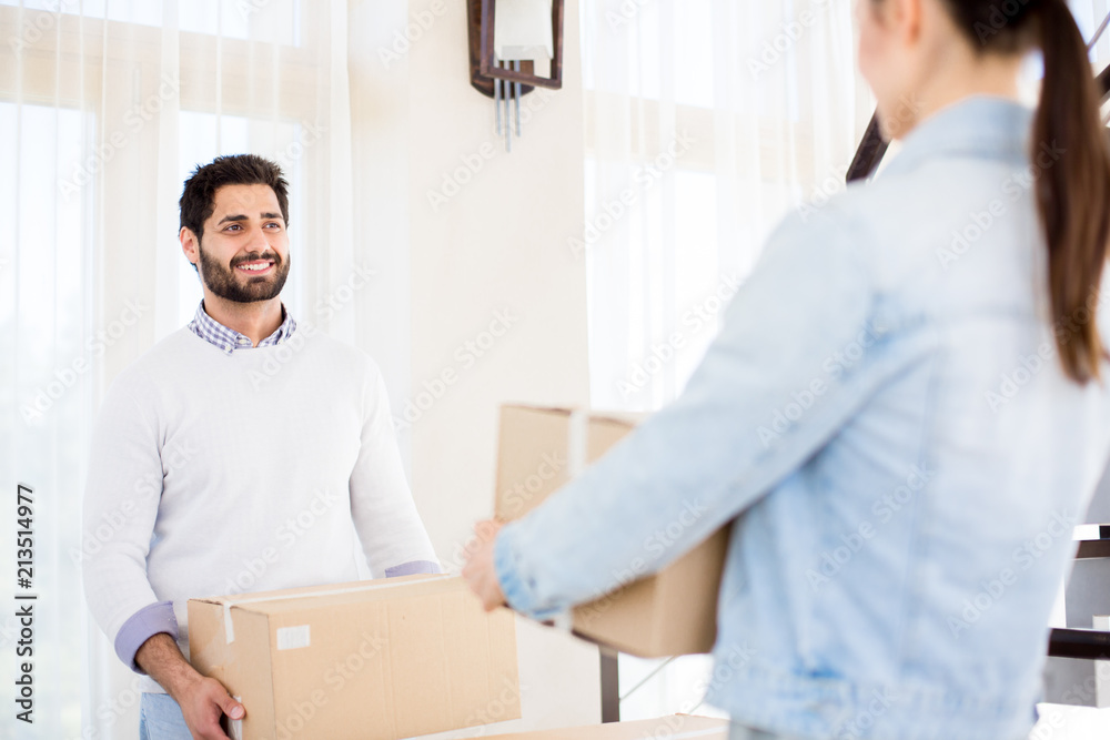 Happy young man and his wife carrying packed boxes with domestic stuff during relocation Happy young man and his wife carrying packed boxes with domestic stuff during relocation