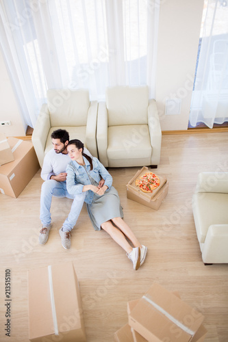 Young restful couple relaxing on the floor of room with three armchairs and several packed boxes