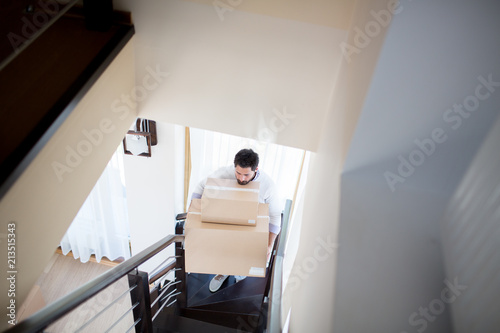 Фотография Young man with big and smaller boxes going upstairs inside new house after reloc
