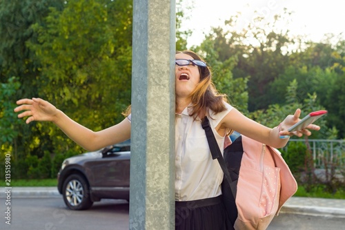 Portrait of young inattentive girl, distracted by mobile phone. Girl crashed into street post, dropped phone. photo