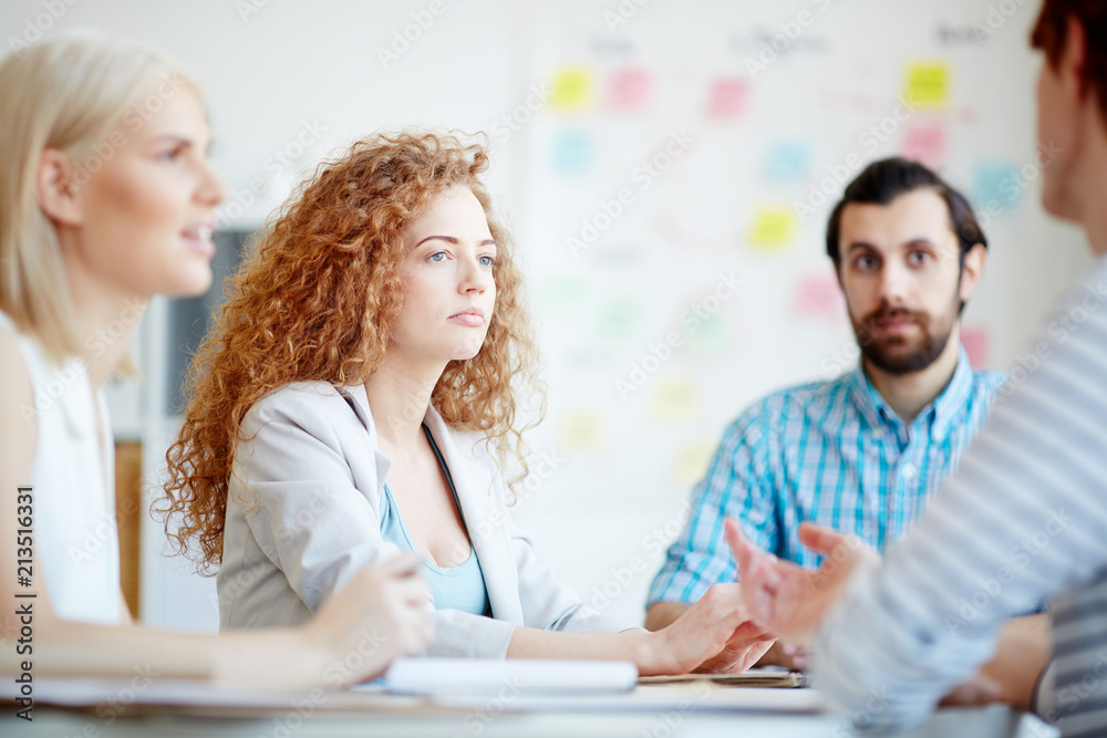 One of businesswomen looking at colleague during discussion of working moments at briefing One of businesswomen looking at colleague during discussion of working moments at briefing